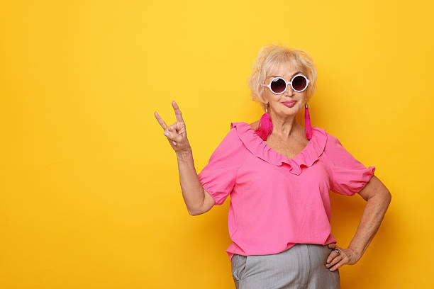 istock Cool grandmother showing rock gesture on orange background. Space for text 2241563158
