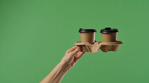 istock Woman Hand Holding Two Coffee Cups with Green Background 2241564679