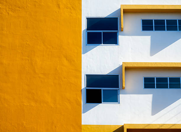 Modern yellow and white building facade with blue glass windows and shadow, minimal architecture background, abstract geometric design with sunlight contrast.