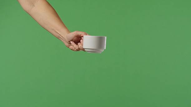 istock Woman Hand Holding White Ceramic Cup on Green Background 2241566466