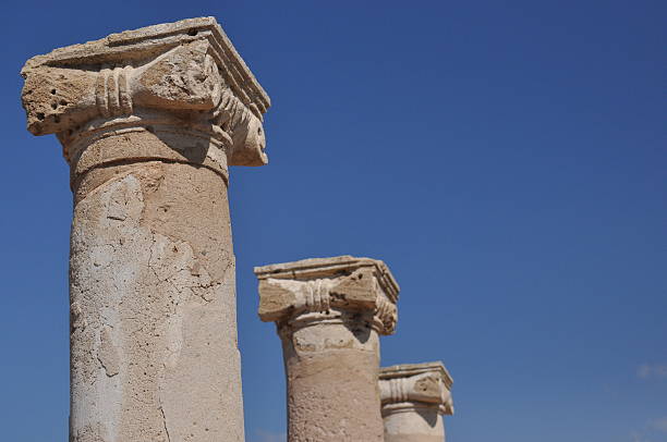 The weathered columns rise majestically under a bright blue sky, showcasing the remnants of a historical site. Sunlight highlights their intricate details, reflecting their ancient glory.