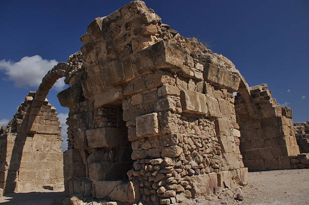 The remnants of ancient stone structures are illuminated by sunlight against a vibrant blue sky. This site evokes a sense of history and architectural significance amidst arid surroundings.