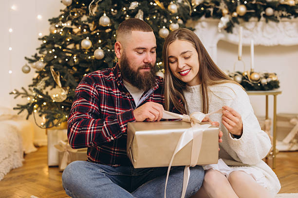 istock Happy couple opening christmas gift next to decorated tree 2241573268