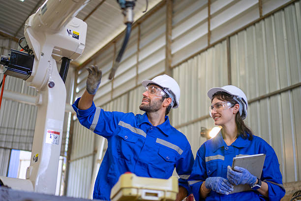 istock Blue collar workers at machine shop with welding robot arm. 2241574122
