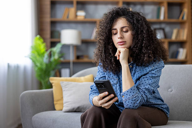 istock Young woman thinking while browsing smartphone at home 2241574133