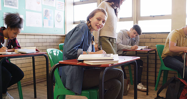 istock Portrait, education and girl in classroom, writing and learning with notebook, test and studying. Knowledge, teenager and student in school, exam and smart with academic lesson and intelligent 2241574394