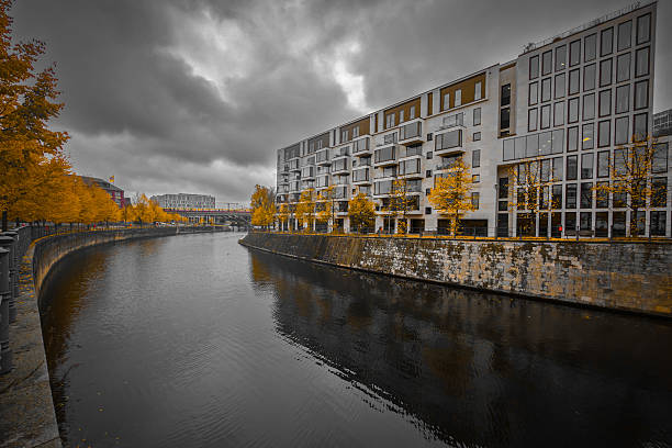 Modern apartment block by the river with yellow autumn trees, dramatic sky reflected in the calm water, urban, melancholic mood, at Berlin Central Station, 10557 Berlin, Germany