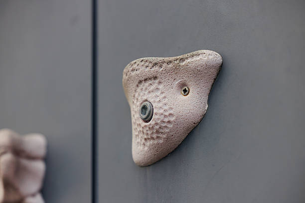 Minimal close-up of colorful indoor climbing holds mounted on a light grey bouldering wall. The holds vary in shape, texture and color. Shot in a modern climbing gym with soft natural light.