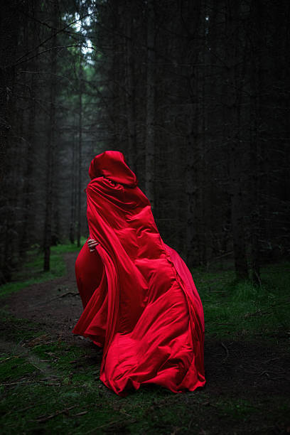 istock woman is seen walking through a dense, dimly lit forest, draped in a long red cloak. atmosphere feels mystical as the fog settles among the trees, creating an enchanting scene 2241577824