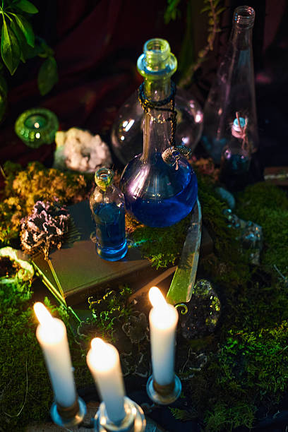 istock table is adorned with various glass bottles filled with blue liquid, surrounded by candles and natural elements. scene captures a mystical, enchanting atmosphere in the dim light 2241577875