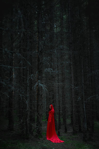 figure draped in a vivid red cloak stands still among tall, shadowy trees in a dense forest at twilight. atmosphere is eerie and enchanting, invoking a sense of wonder and curiosity