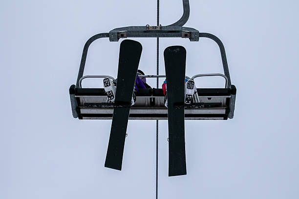 Skier is using a chairlift to ascend a mountain slope with ski equipment on a cloudy winter day