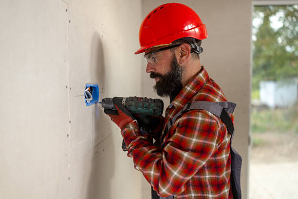 istock Bearded male construction worker installing electrical outlet in wooden house under construction with power drill 2241581565