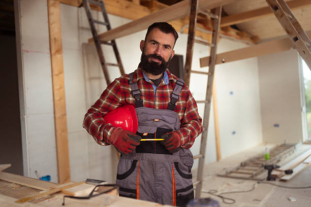 istock Construction Worker Holding Red Helmet Inside Wooden House Under Construction Wearing Work Overalls 2241581622