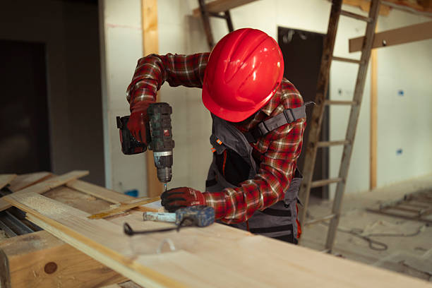 Portrait of happy worker making funny face and drill wall in room. Man in protective yellow helmet and glasses. Construction site and renovation in apartment concept