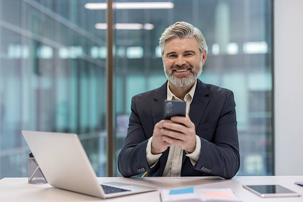 istock Smiling businessman using smartphone at office desk 2241586870