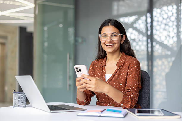 istock Young indian woman smiling using smartphone in office 2241588000