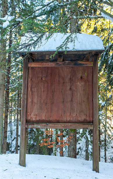 Blank wooden information board standing in a snowy Italian forest, offering copy space for various messages or announcements amidst the tranquil winter landscape