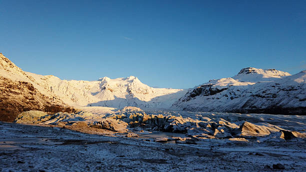Expansive glacial terrain and snow-covered mountains reflecting the golden hour light, highlighting the dramatic natural features of the Icy landscape during a cold day
