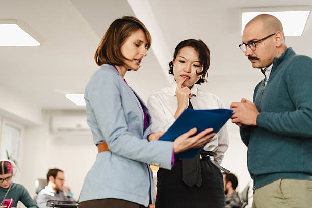 istock Businesspeople discussing project details in a modern office setting during a weekday meeting with team members in the background 2241591177