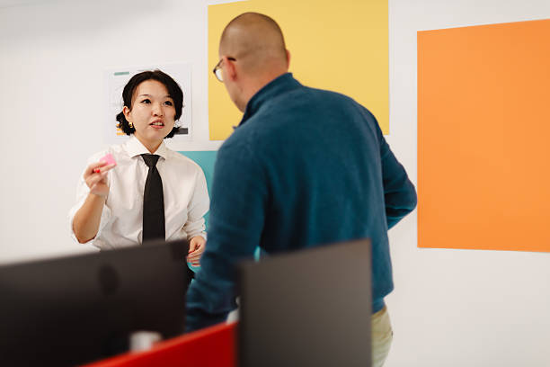 Business meeting between two professionals in modern office space discussing ideas during afternoon hours with colorful wall accents in the background