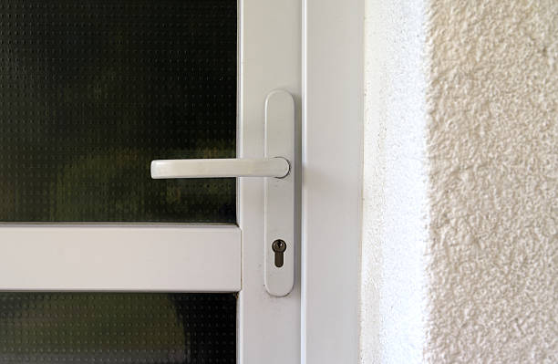 istock Sleek white door handle mounted on a textured metal-and-glass surface, featuring a secure lock mechanism. The surrounding stucco wall and frame add contrast to this modern architectural detail. 2241593066