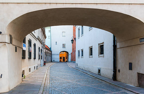 Warsaw, Poland – May 25, 2025: A bright stone arch frames a quiet cobbled alley, opening into a courtyard beyond. Evening light adds depth to the soft tones of old town architecture.