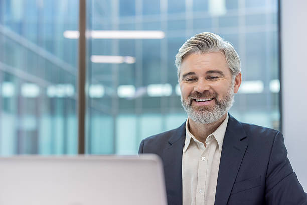istock Senior businessman smiling, working on laptop in modern office 2241598524