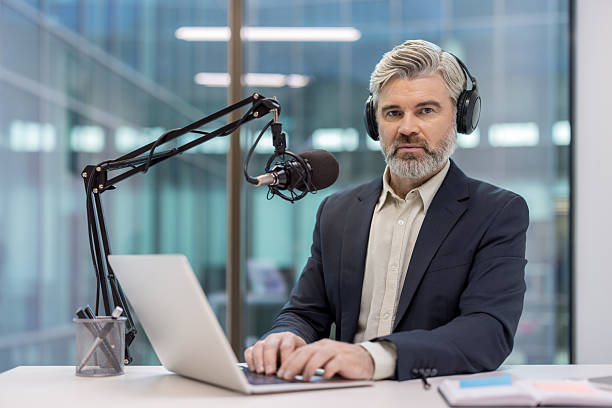 istock Mature man broadcasting podcast, operating recording equipment, looking at camera 2241600738