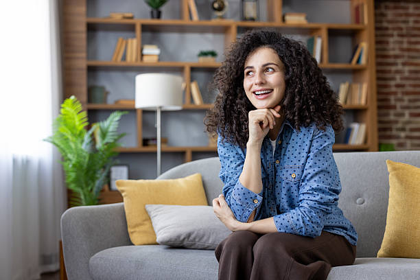 istock Young woman daydreaming smiling on sofa at home 2241612549