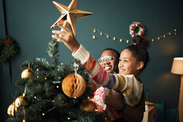 istock Black Man Lifting Smiling Child Decorating Christmas Tree with Ornaments Indoors 2241613203