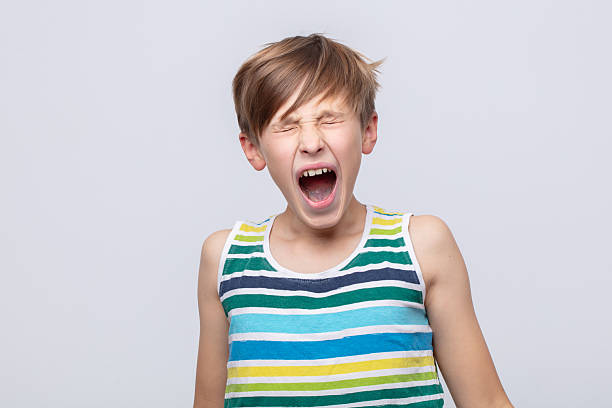 Young boy expressing excitement while shouting in a striped tank top against a plain background