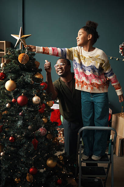 istock Young Black Girl Decorating Christmas Tree with Smiling Middle Aged Black Man 2241620057