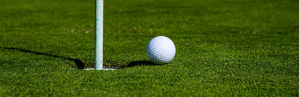 istock Golf ball on lip of cup on grass background. Golf hole. 2241621315