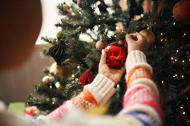 istock Young Black Woman Decorating Christmas Tree with Red Ornament during Holiday 2241623111