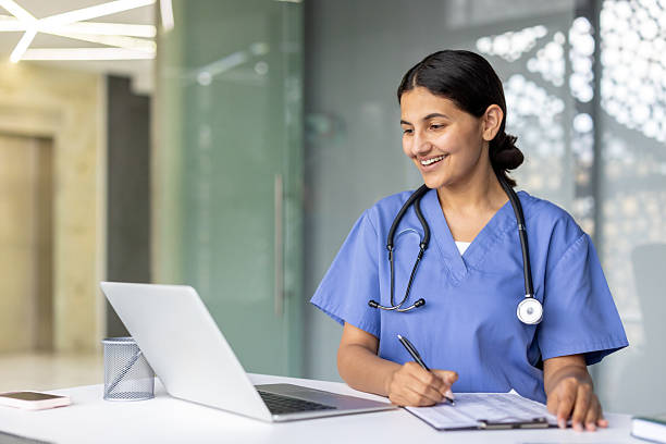 istock Smiling female doctor working on laptop and writing notes 2241623625