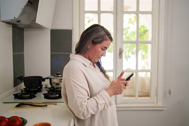 istock Woman drinking coffee and using smartphone in modern kitchen 2241625477