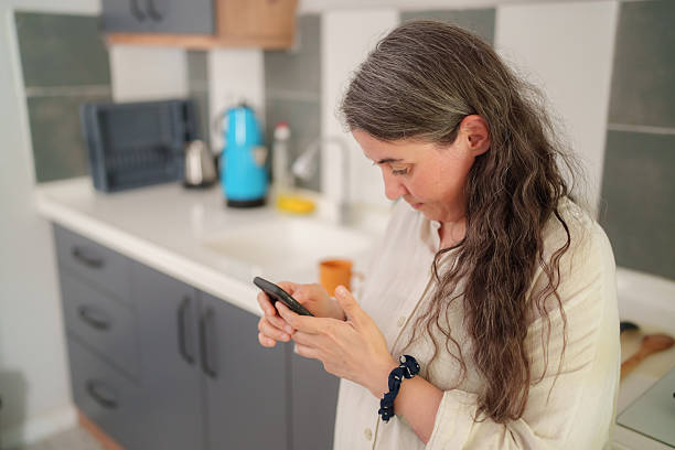 istock Woman drinking coffee and using smartphone in modern kitchen 2241625731