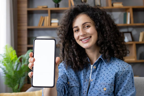 istock Smiling woman showing smartphone with blank screen at home 2241626623