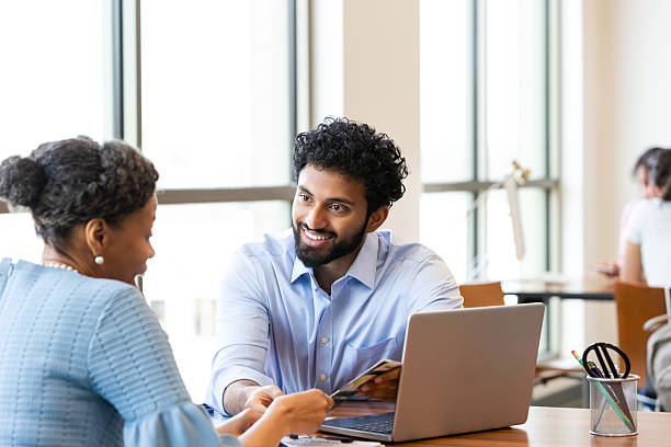 istock Two professionals engage in discussion while collaborating over documents and a laptop in an office setting. 2241629889