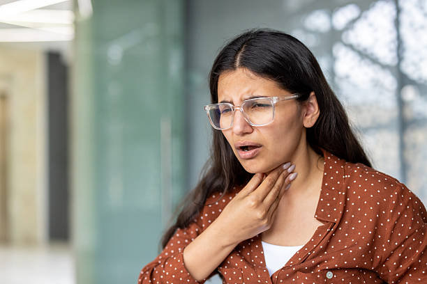 istock Young woman suffering from sore throat touching neck 2241631235