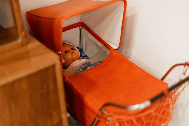 A vintage doll lies quietly in a bright orange stroller, surrounded by a warm and inviting room setting, highlighting a nostalgic atmosphere.