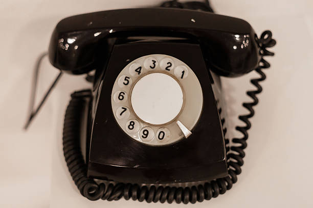 istock A classic rotary phone with a circular dial and coiled cord rests on a flat, smooth surface. The black exterior adds a nostalgic touch, reminiscent of mid-20th century communication 2241631536