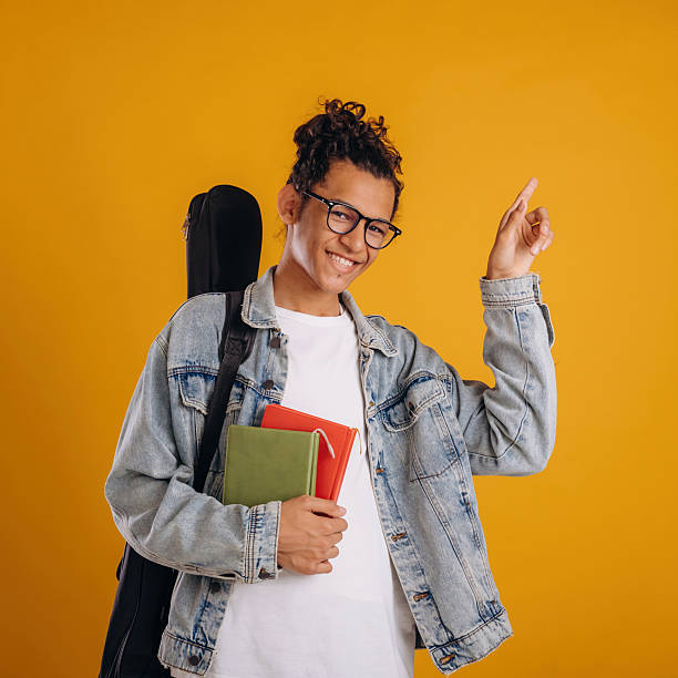 istock Guitar backpack on back and notepads in hand. Young guy is against yellow background 2241639013