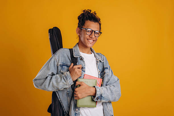 istock Guitar backpack on back and notepads in hand. Young guy is against yellow background 2241639022