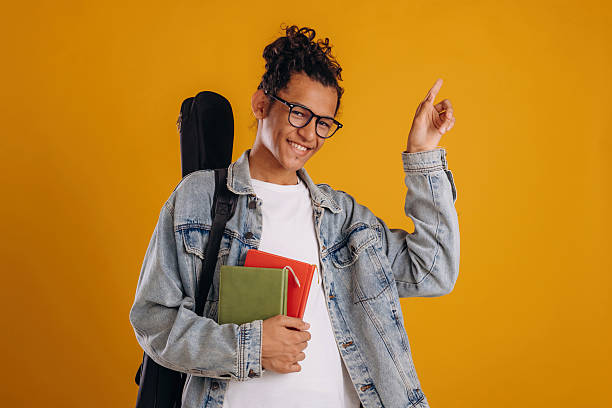 istock Guitar backpack on back and notepads in hand. Young guy is against yellow background 2241639028