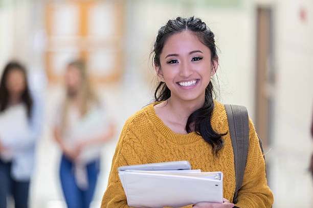 istock Young, smiling female student walks down hallway carrying books and a tablet. 2241640100