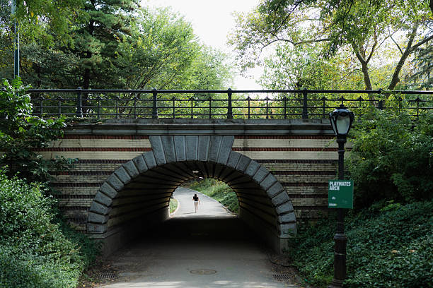 Woman walking a path through the playmates arch tunnel on a bright day in central park, new york city