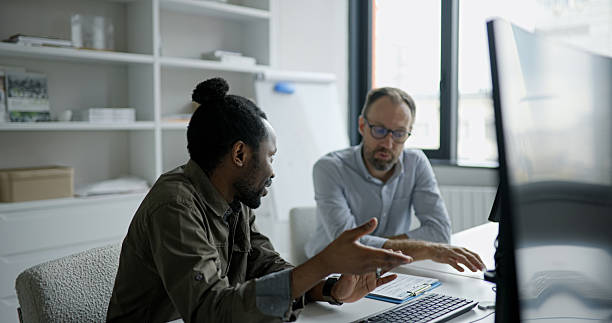 istock Two men in a modern office discuss a project at a laptop desk during a meeting 2241641474