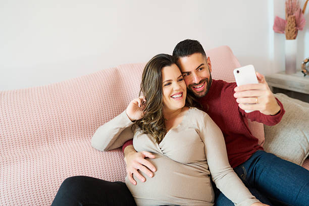 istock Pregnant couple sharing happy selfie on sofa 2241644400
